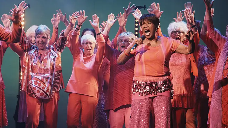 Ein Chor mit älteren Frauen singt begeistert auf einer Bühne.